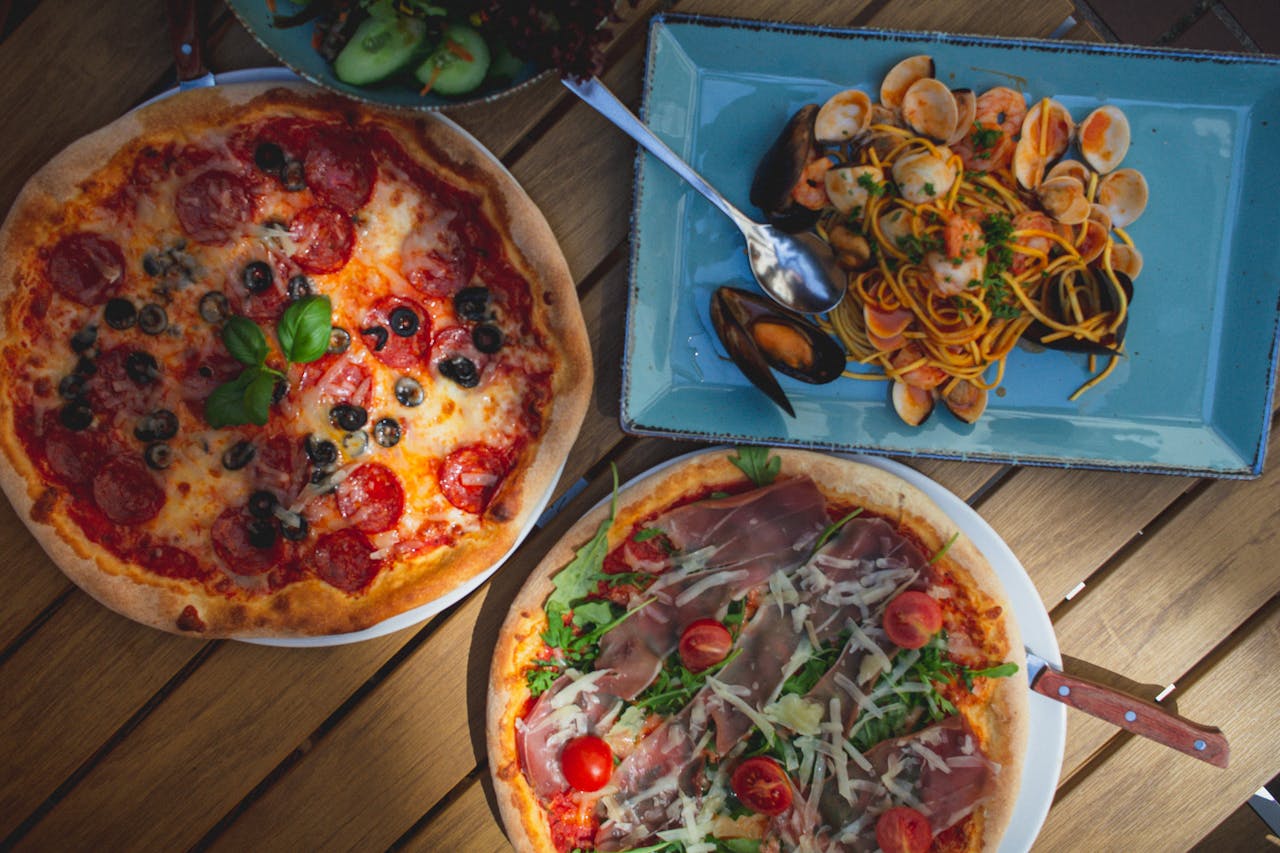services-03 Top view of delicious pizzas and seafood pasta, perfect for Italian food enthusiasts. Captured in natural light.
