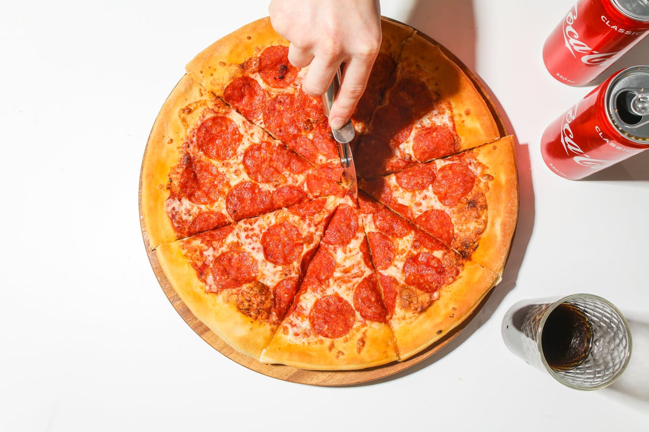 services-02 A delicious pepperoni pizza being sliced with classic soda cans for a tasty meal.